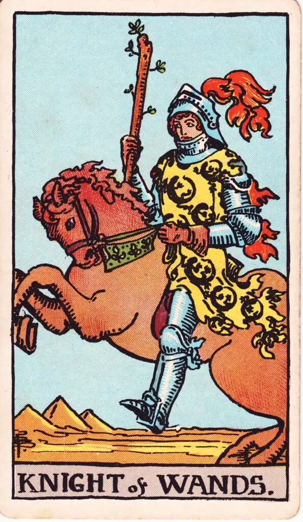 Illustration du Cavalier de Bâtons du tarot Rider-Waite : un chevalier en armure monte un cheval au galop dans le désert, brandissant un bâton fleuri, symbole d’audace, de passion et de mouvement rapide.