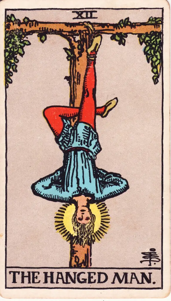 Carte du Pendu dans le tarot Rider-Waite : un homme suspendu par un pied à une branche en forme de tau, la tête en bas, auréolé de lumière. Illustration de 1909 par Pamela Colman Smith.