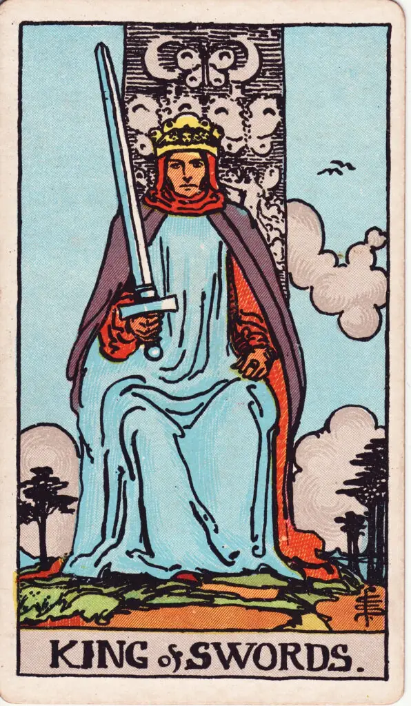 Illustration du Roi d’Épées du tarot Rider Waite : un roi trône, tenant une épée dressée dans la main droite, son regard est droit et déterminé, le ciel est clair, décoré de nuages et d’oiseaux.