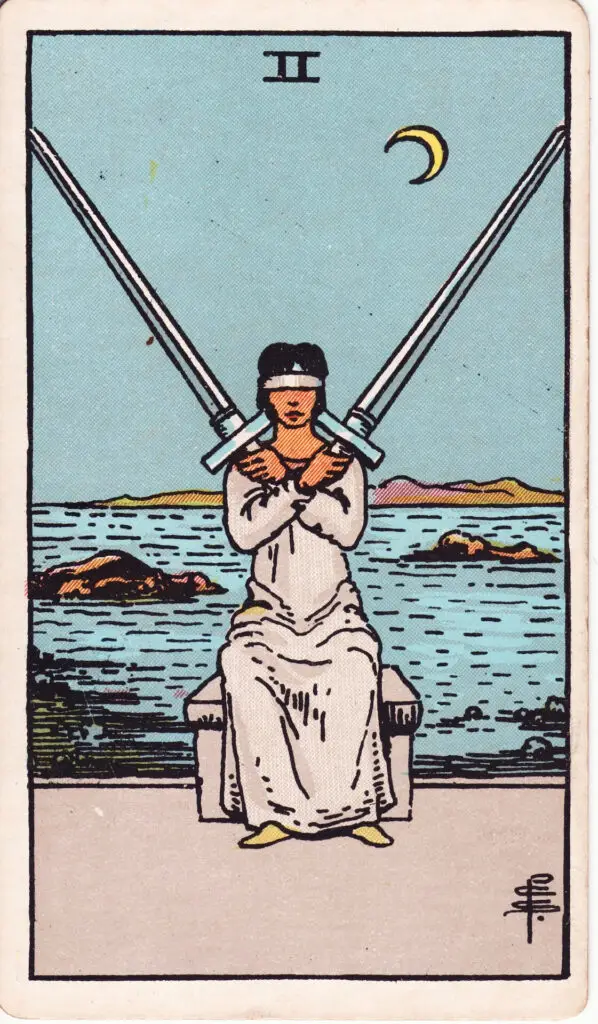 Illustration du Deux d’Épées du tarot Rider Waite : une femme assise, les yeux bandés, tient deux épées croisées sur sa poitrine, assise devant une mer calme sous un croissant de lune.