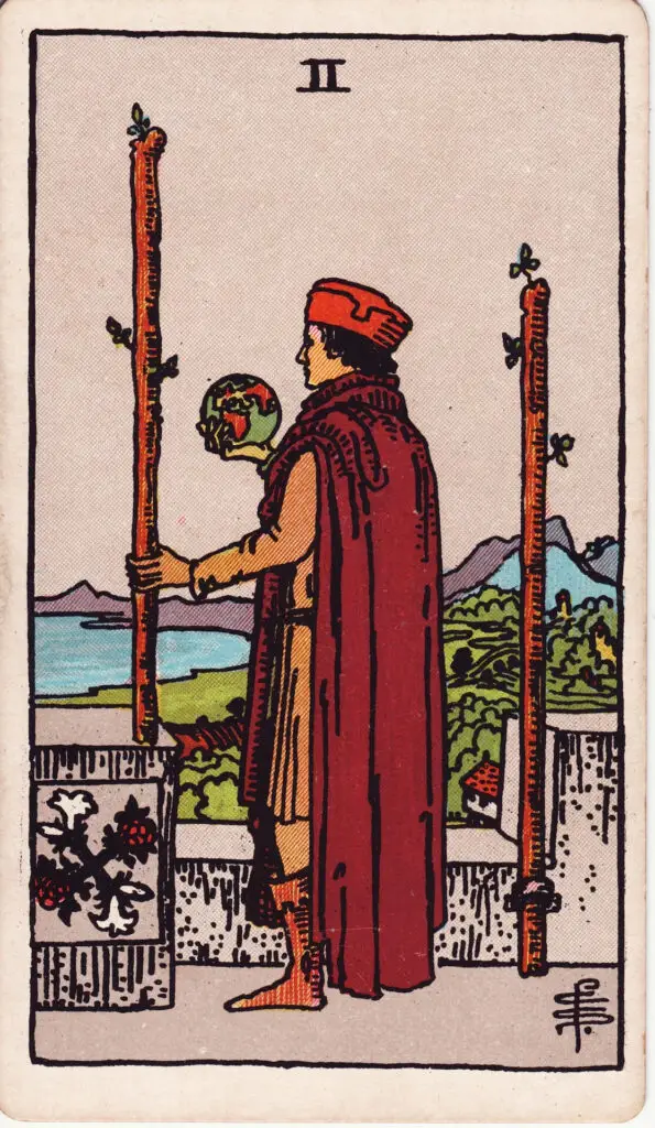 Illustration du Deux de Bâtons du tarot Rider-Waite : un personnage tient un globe terrestre et regarde vers l’horizon depuis les hauteurs d’un château, entre deux bâtons.