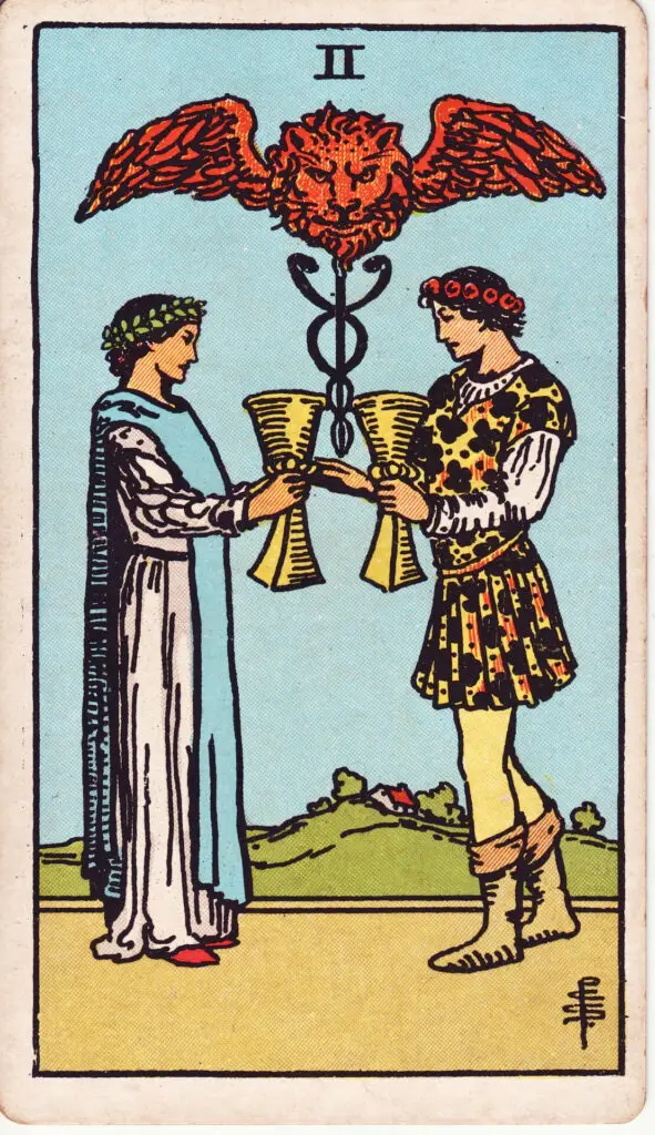 Illustration du Deux de Coupes du tarot Rider Waite : un homme et une femme se tiennent face à face et échangent des coupes, sous un caducée ailé surmonté d’un lion à tête flamboyante.