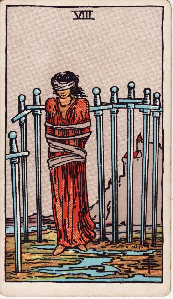 Illustration du Huit d’Épées du tarot Rider Waite : une femme aux yeux bandés est entourée de huit épées plantées dans le sol, les bras liés, debout sur un sol humide.